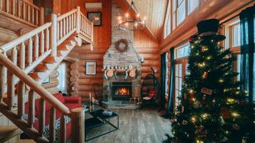 A log cabin interior with a fireplace, a Christmas tree, and a staircase.