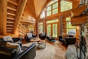 Een houten blokhut interieur met een open haard, meerdere zithoeken en grote ramen.