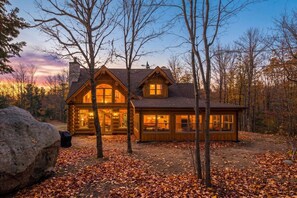 A log cabin with a prominent chimney, large windows, and a porch area.