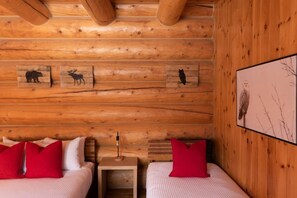 A log cabin room with two beds, a nightstand, and wall-mounted artwork of animals. - Private Hot Tub / Sauna / Indoor Pool / Nyctale (Mille-Isles)
