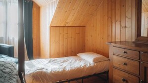 Ein Zimmer mit einem Bett, Holzwänden, einem Schminktisch und einem Fenster mit Vorhängen.