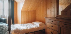 Een kamer met een bed, houten wanden, een dressoir en een raam met gordijnen.