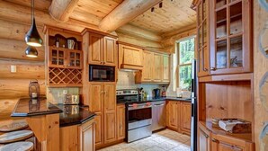 Interior de una cabaña de madera con área de cocina que incluye armarios de madera, un microondas, una estufa y un refrigerador.