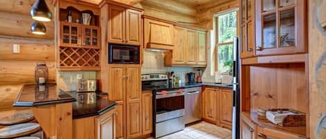 Interior de una cabaña de madera con área de cocina que incluye armarios de madera, un microondas, una estufa y un refrigerador.
