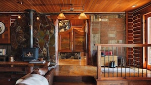 A cozy cabin interior with a stone fireplace, wooden walls, and a staircase leading to a loft area.