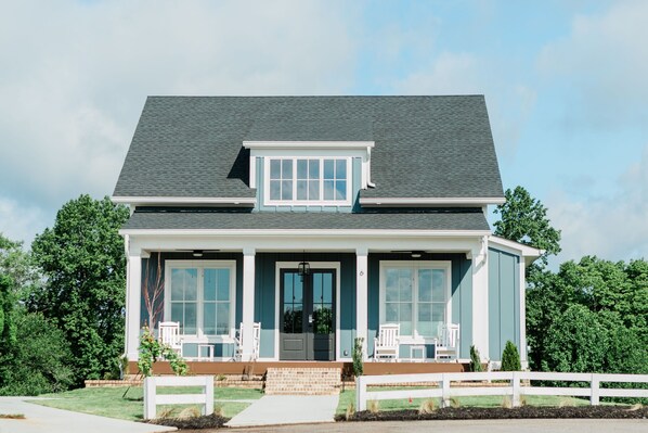 A two-story house with a front porch, a small attached garage, and a fenced yard. - Kaya Cottages (Cleveland)