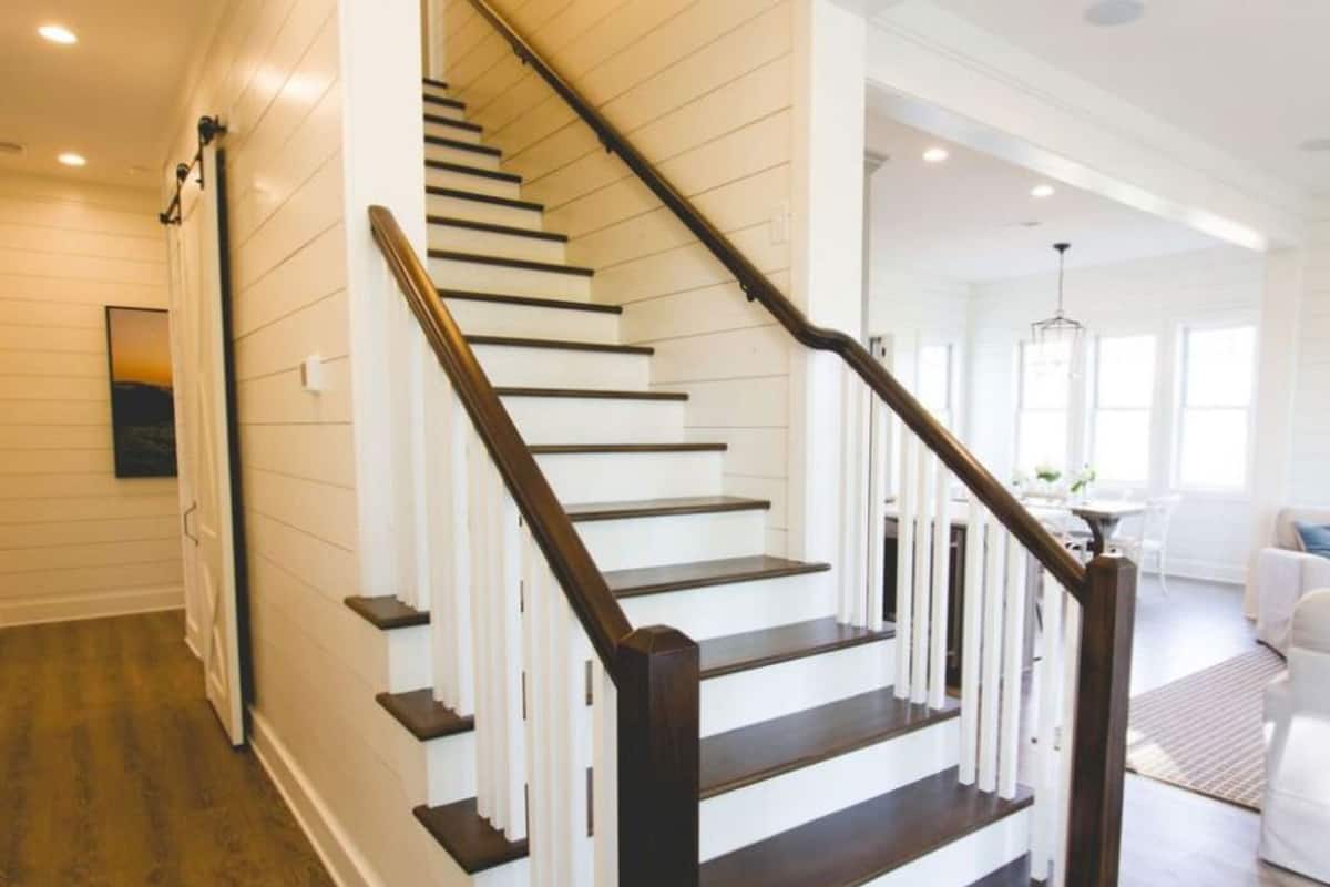 Una escalera con escalones de madera oscura y paredes blancas que conduce a un espacio interior luminoso.