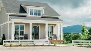 A two-story house with a covered porch, large windows, and a view of mountains in the background. - Kaya Cottages (Cleveland)