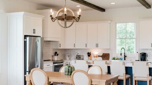 A modern kitchen with white cabinetry, a stainless steel refrigerator, a wooden dining table with chairs, and a chandelier. - Kaya Cottages (Cleveland)