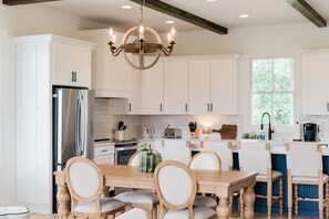 A modern kitchen with white cabinetry, a stainless steel refrigerator, a wooden dining table with chairs, and a chandelier. - Kaya Cottages (Cleveland)