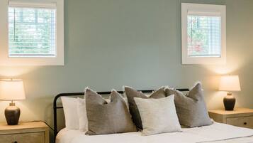 A neatly made bed with white and gray pillows, two bedside lamps, and a window with blinds.