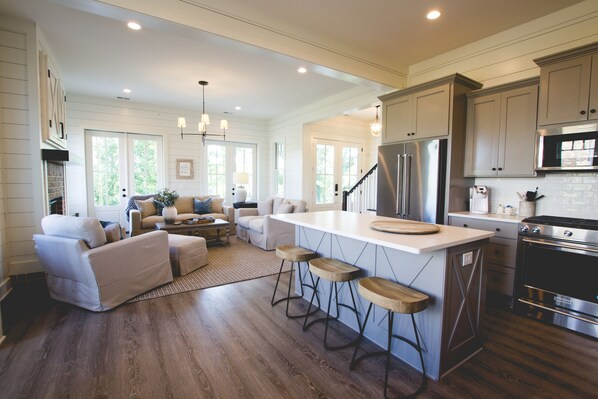 A spacious kitchen with wooden flooring, a central island with stools, stainless steel appliances, and a cozy seating area with a sofa and coffee table. - Kaya Cottages (Cleveland)