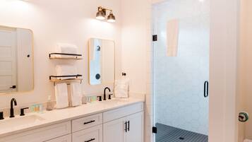 A modern bathroom with a white vanity, two mirrors, a glass shower enclosure, and a hexagonal tile backsplash.