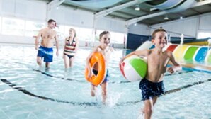 An indoor swimming pool with clear lanes, a colorful ceiling, and a lifeguard stand. - Evergreen Pines Cayton Bay Holiday Park (Scarborough)