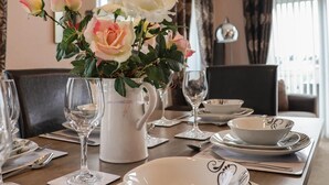 A dining table set with white plates, bowls, and cutlery, a pitcher, and a vase with roses. - Evergreen Pines Cayton Bay Holiday Park (Scarborough)