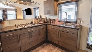 A modern kitchen with dark wood cabinets, a stainless steel sink, and a gas stove. - Evergreen Pines Cayton Bay Holiday Park (Scarborough)