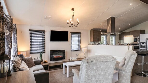 A modern living room with a flat-screen TV, fireplace, and a dining area with a bar. - Evergreen Pines Cayton Bay Holiday Park (Scarborough)