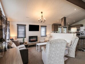 A modern living room with a flat-screen TV, fireplace, and a dining area with a bar. - Evergreen Pines Cayton Bay Holiday Park (Scarborough)