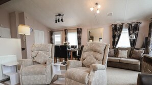 A living room with two armchairs, a sofa, a dining table with chairs, and a coffee table. - Evergreen Pines Cayton Bay Holiday Park (Scarborough)