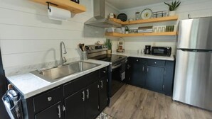 A modern kitchen with black cabinets, stainless steel appliances, wooden shelves, and a marble countertop. - Mountain Cabin in Jamestown (Jamestown)