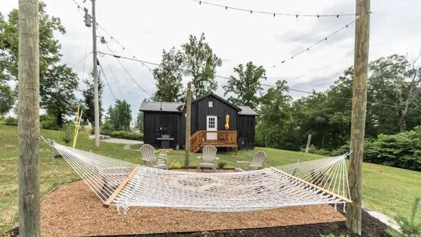 A hammock set up in a garden with a wooden deck and chairs, surrounded by trees and a house in the background. - Mountain Cabin in Jamestown (Jamestown)