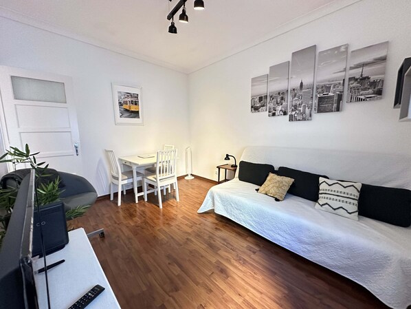 A modern, well-lit room with a wooden floor, a white sofa, a dining table with chairs, a TV, and a radiator. - Central Lisbon by Trip2Portugal (Lisbon)