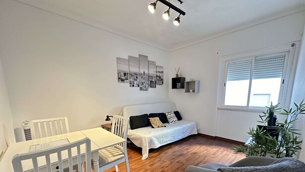 A modern living room with a white sofa, a dining table with chairs, a grey armchair, and a large window with blinds. - Central Lisbon by Trip2Portugal (Lisbon)