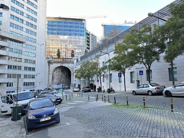 Eine gepflasterte Straße mit parkenden Autos, ein blaues Auto im Vordergrund und ein Steinbogen.