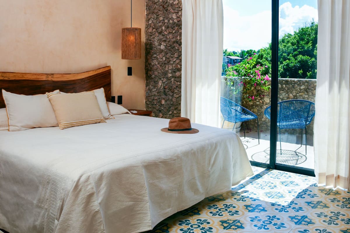 Une chambre avec un grand lit, un mur en pierre, un balcon avec des chaises et un sol à motifs.