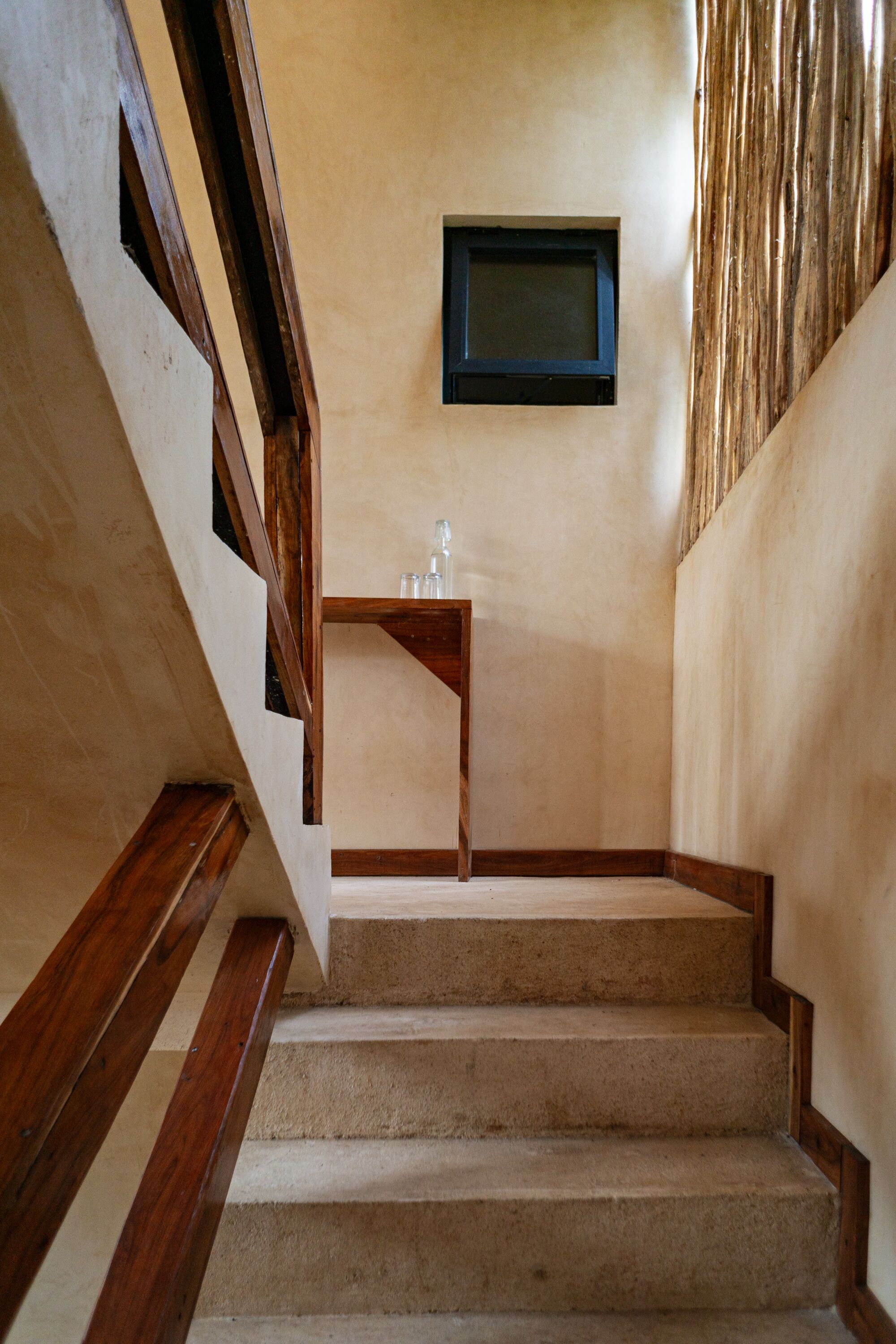A staircase with wooden handrails and beige carpeted steps leading to a landing with a small table and a framed picture on the wall.