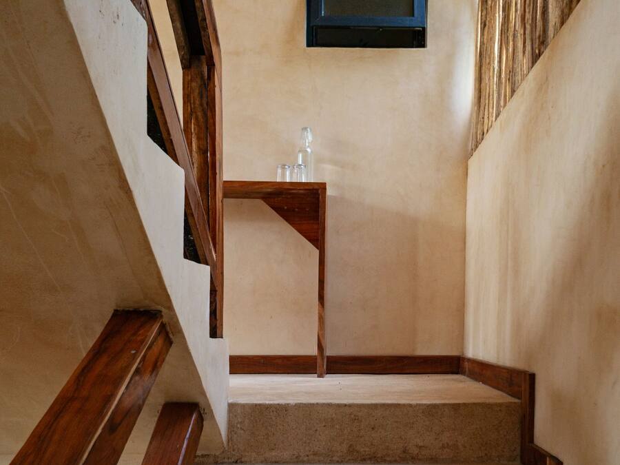 A staircase with wooden handrails and beige carpeted steps leading to a landing with a small table and a framed picture on the wall.