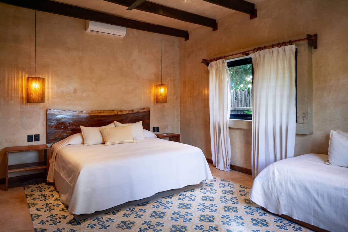 Une chambre à coucher avec un grand lit, deux tables de chevet, une fenêtre avec des rideaux et un sol à motifs.