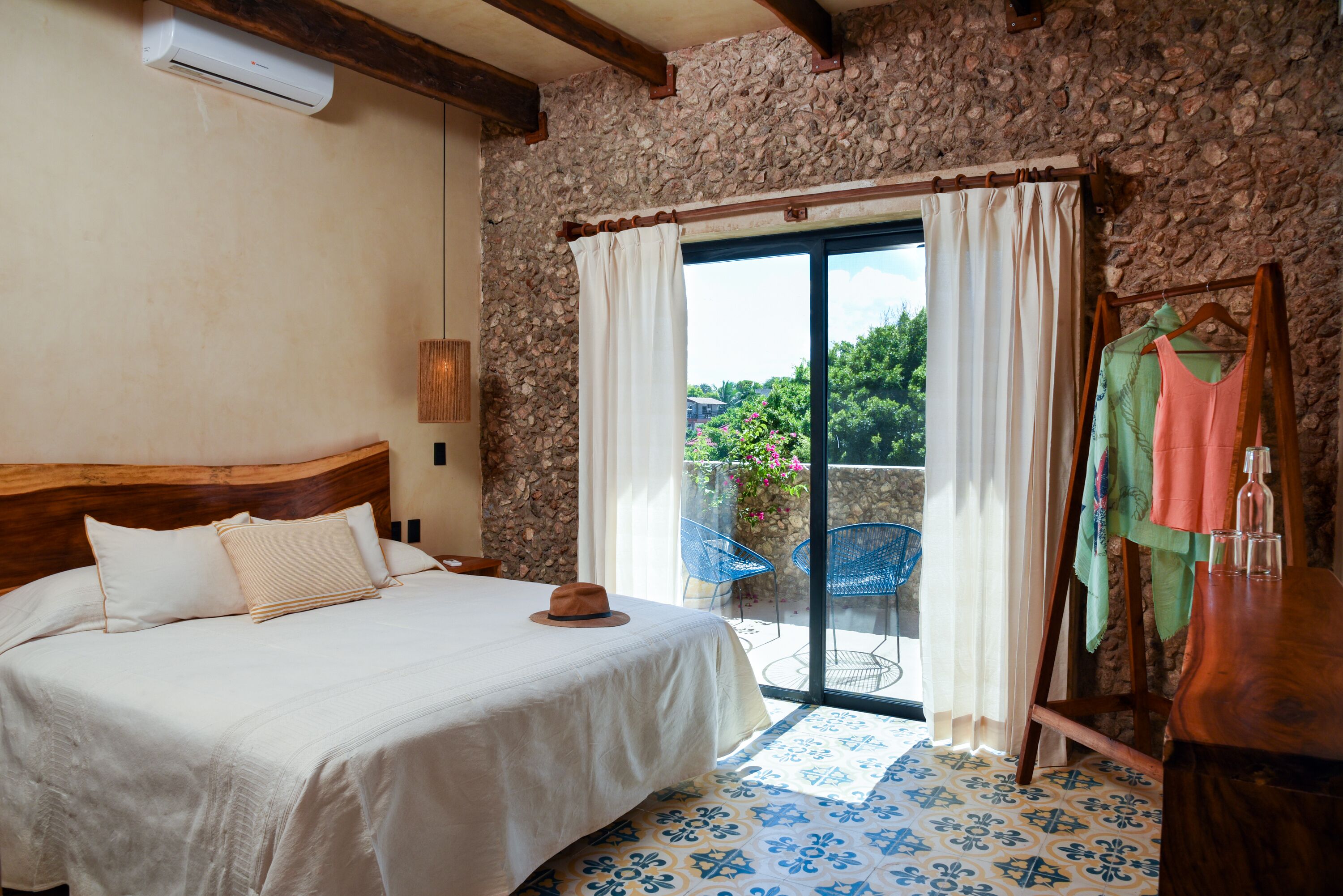 Un dormitorio con cama, ventana con cortinas, pared de piedra y vista a espacios verdes.