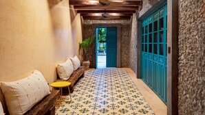 A hallway with a patterned floor, a wooden bench with cushions, a small round table, and a blue door. - Mero Mero Hotel (El Cuyo)