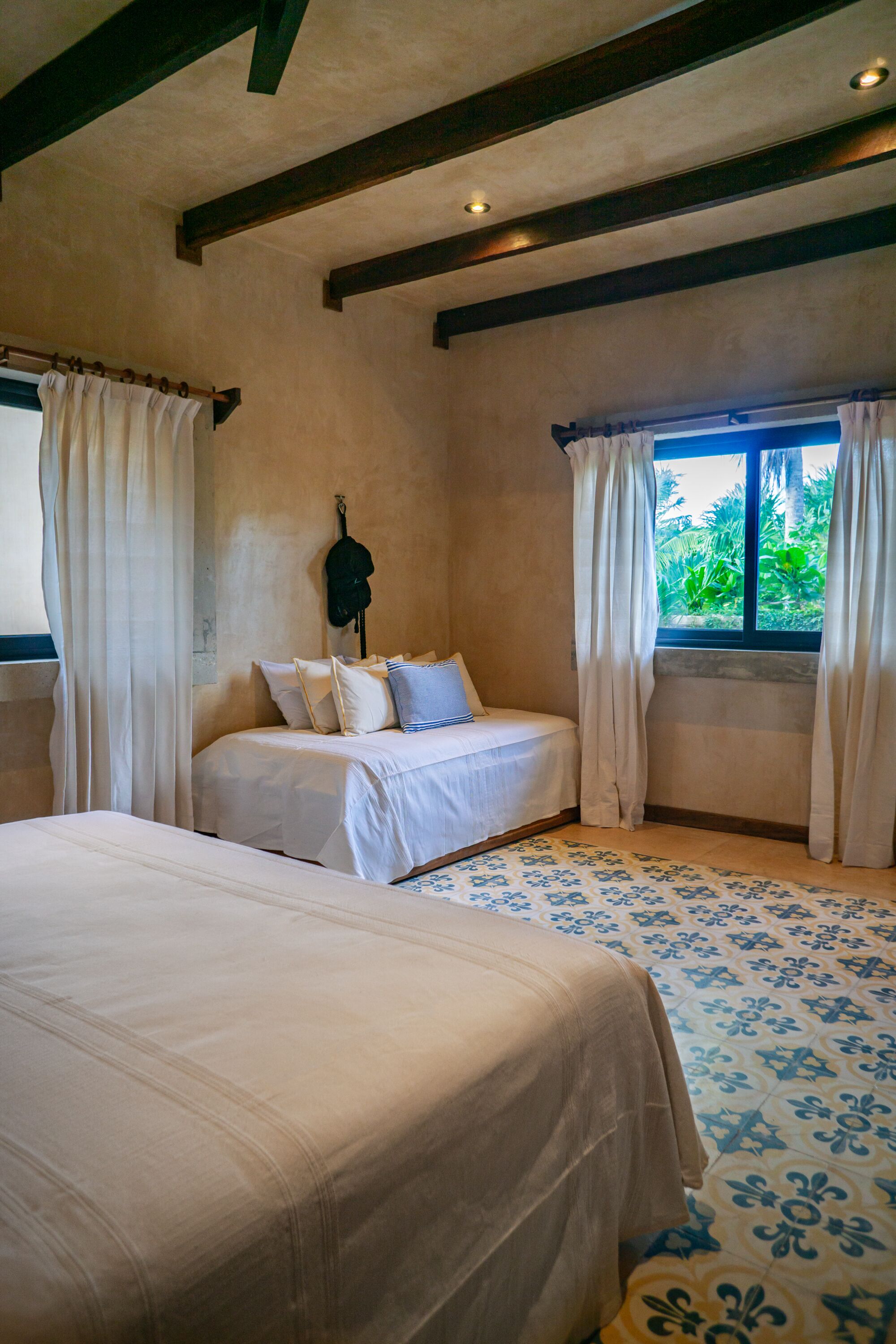 A bedroom with a large bed, a smaller bed, and a window with curtains.