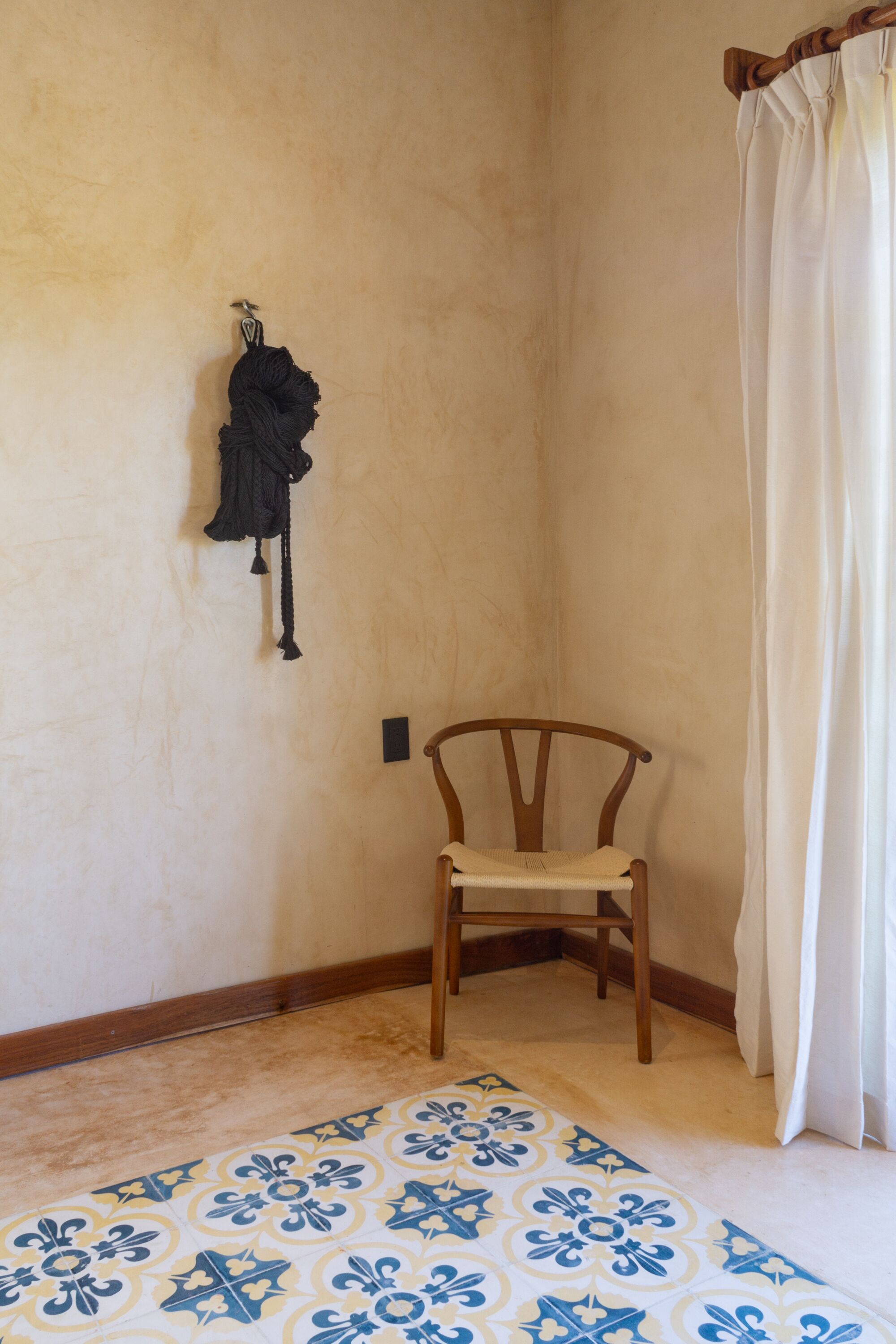Une pièce d’angle avec une chaise en bois, un tapis à motifs, un rideau et un crochet fixé au mur.