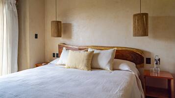 A neatly made bed with white linens and two pillows, a wooden headboard, and two hanging pendant lights.
