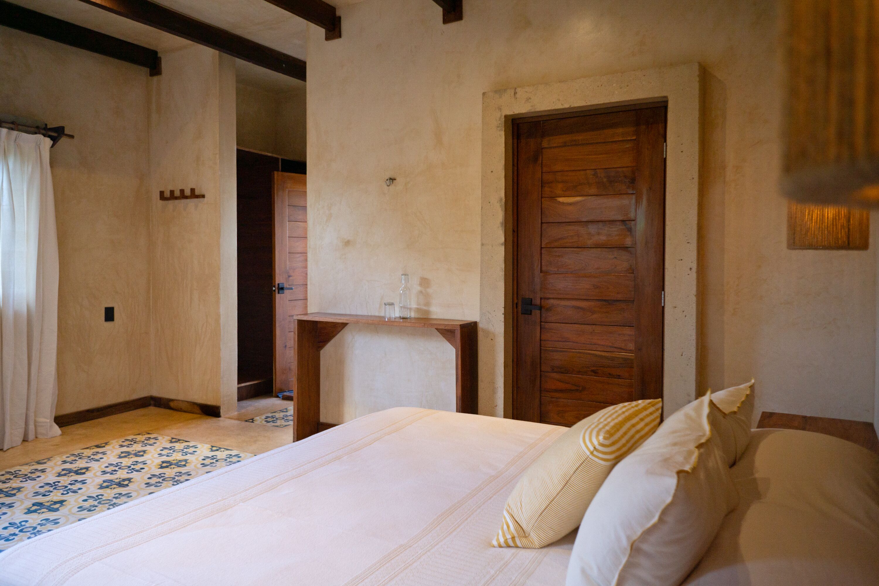 Un dormitorio con una cama, una puerta de madera y una pequeña mesa de madera.