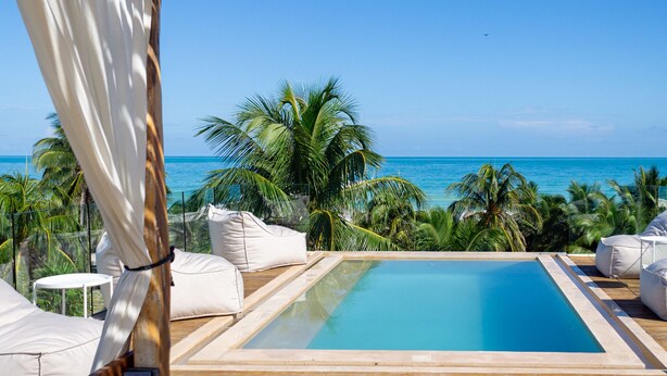 A pool area with a view of the ocean, surrounded by palm trees and white furniture. - Mero Mero Hotel (El Cuyo)