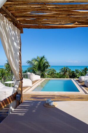 A pool area with a view of the ocean, surrounded by palm trees and white furniture. - Mero Mero Hotel (El Cuyo)