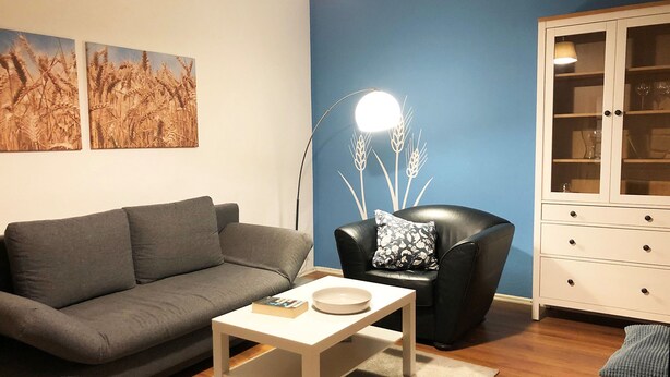 A living room with a grey sofa, a white coffee table, a black armchair with a floral pillow, a floor lamp, and a cabinet with glass doors. - Apartment Kornkammer near Lake Plau (Halenbeck-Rohlsdorf)