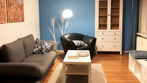 A living room with a sofa, a black leather chair, a white cabinet, and a floor lamp. - Apartment Kornkammer near Lake Plau (Halenbeck-Rohlsdorf)