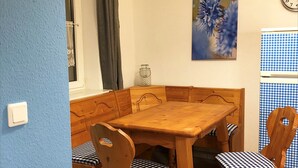 A dining area with a wooden table and chairs, a window with curtains, a wall clock, and a painting. - Apartment Kornkammer near Lake Plau (Halenbeck-Rohlsdorf)