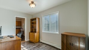 Une pièce avec un bureau en bois, une bibliothèque intégrée, un radiateur et une fenêtre avec des stores.
