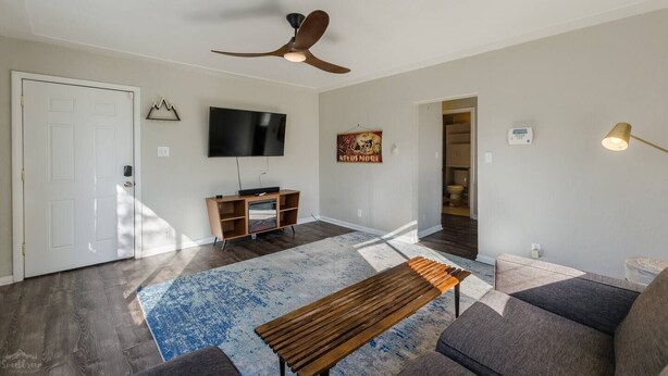 Un salon moderne doté d’un téléviseur à écran plat, d’un meuble de rangement en bois et d’un ventilateur de plafond.