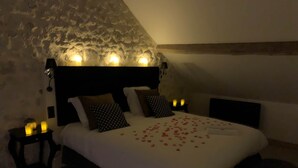 Un dormitorio acogedor con una pared de piedra, un cabecero de madera y una cama decorada con pétalos de rosa.