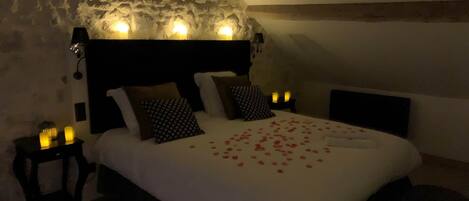 A cozy bedroom with a stone wall, a wooden headboard, and a bed adorned with rose petals.