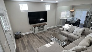 A modern living room with a large sectional sofa, a flat-screen TV, and a dining area with a kitchen in the background. - PERFECT - LARGE CUSTOM HOME - Completely Renovated, Beautiful Fenced in Yard!!!! (Indianapolis)