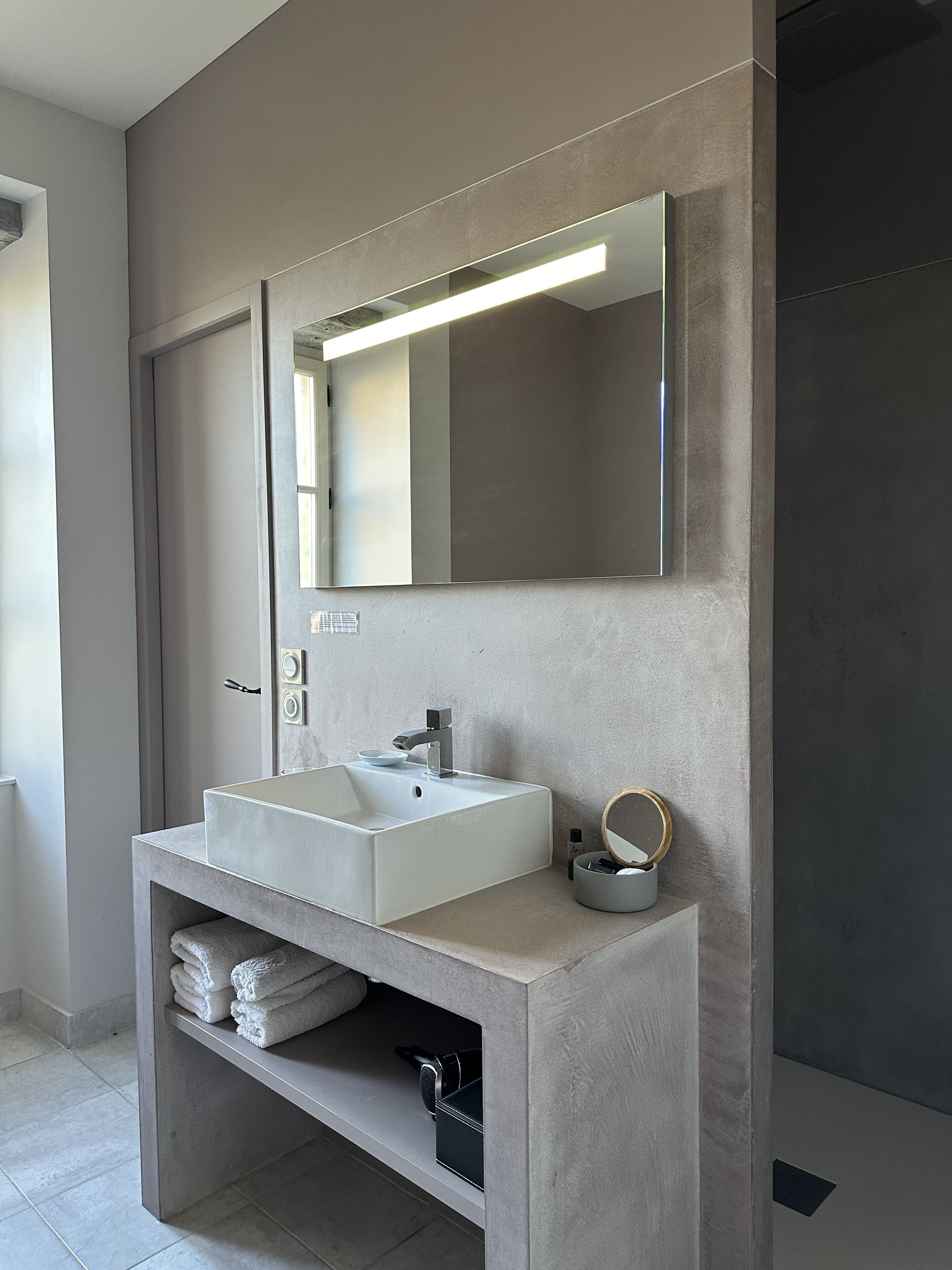 A modern bathroom with a rectangular sink, a large mirror, and a towel shelf.