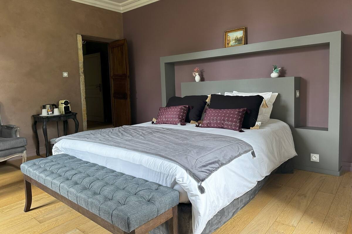 Ein Schlafzimmer mit einem großen Bett, einem Nachttisch, einer Bank und einer Tür zu einem anderen Raum.